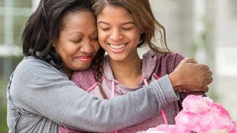 African-American mother hugging her middle school girl, both smiling